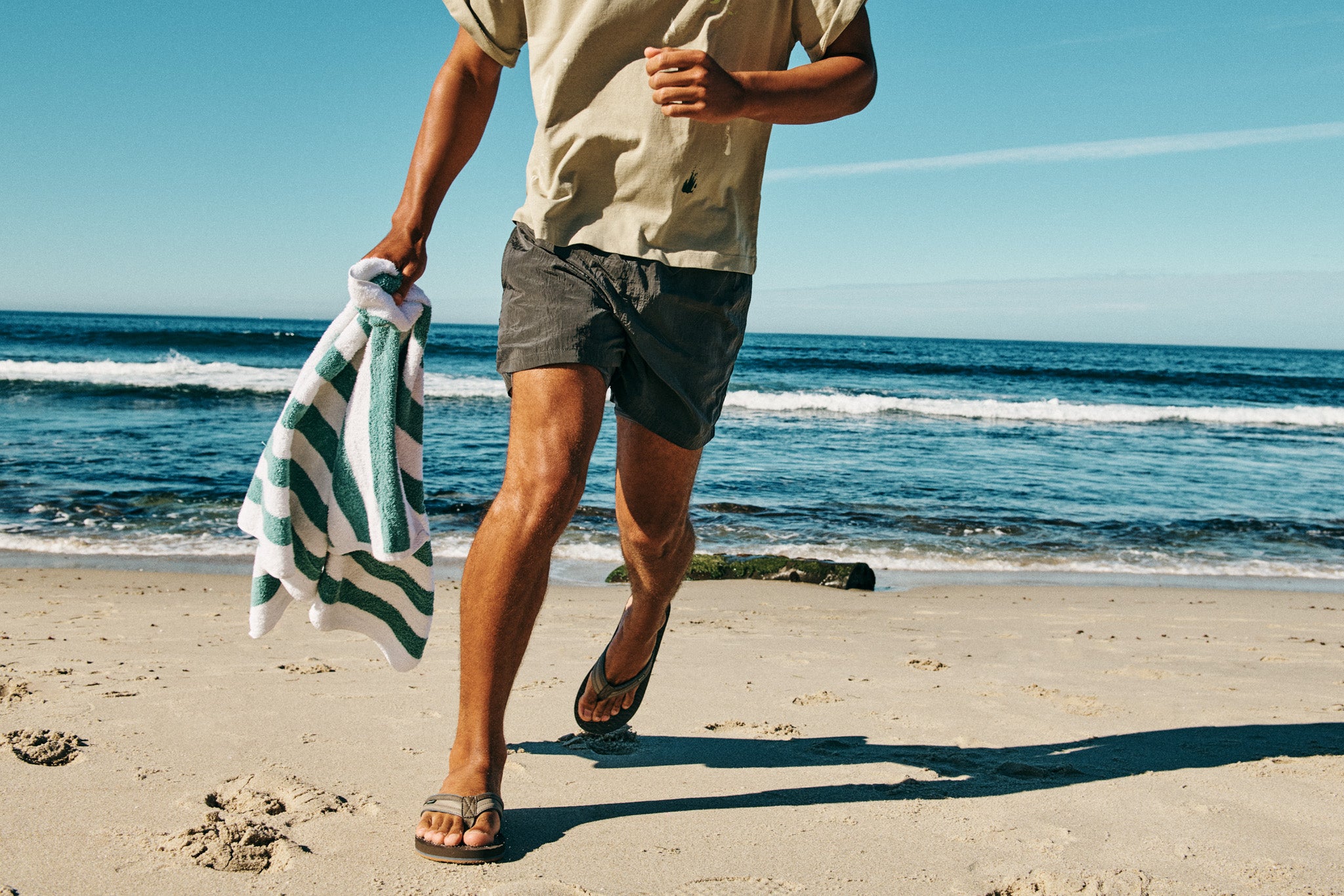 Man wearing Ziggy men's sandals runs along the sandy beach, capturing a relaxed and effortless summer vibe.